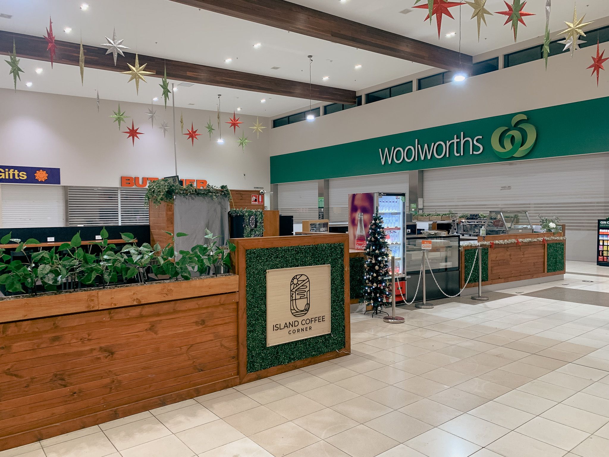 Island Coffee Corner kiosk interior with branded timber counter, moss wall, and Woolworths in background