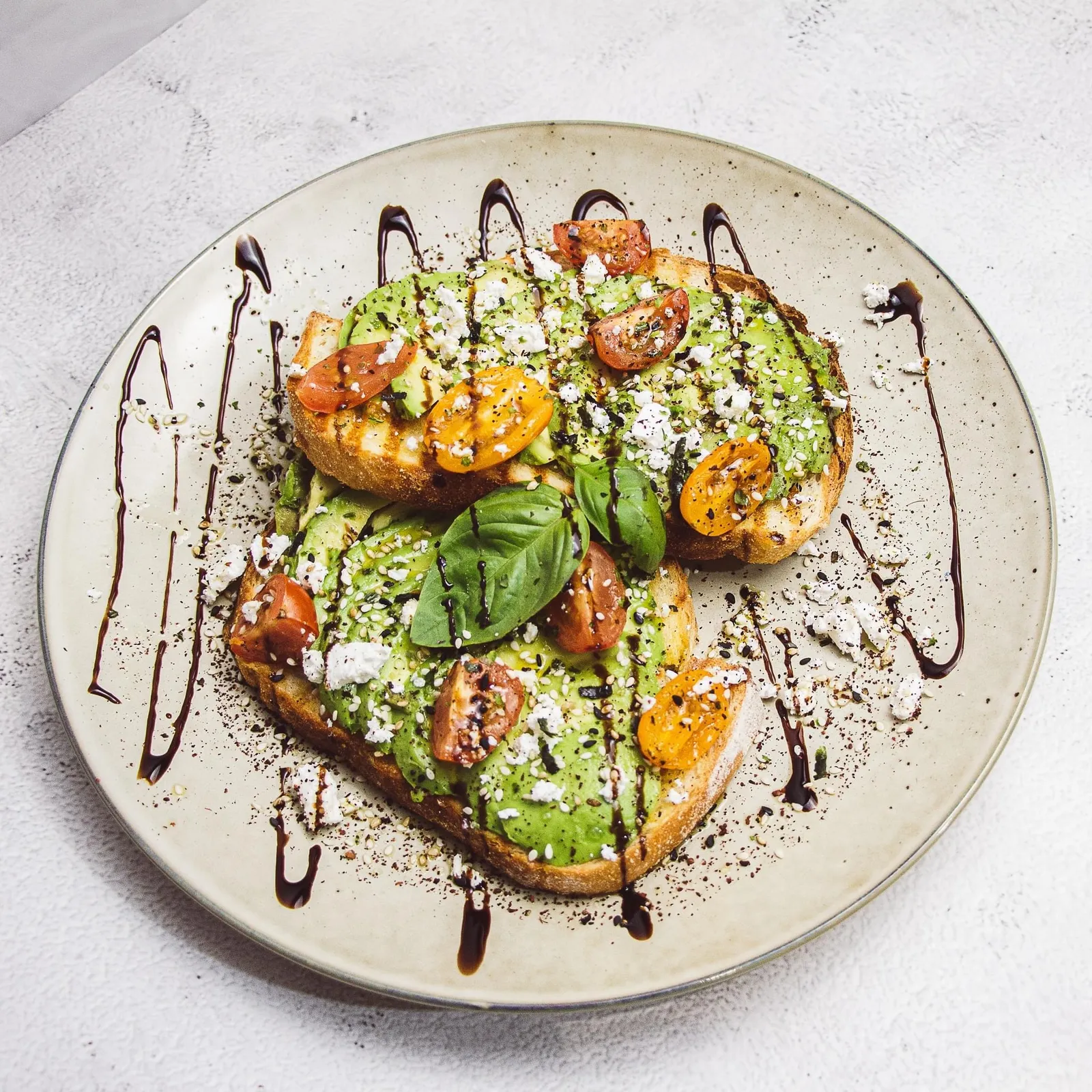 Smashed avocado toast with cherry tomatoes, feta, and balsamic glaze on ceramic plate