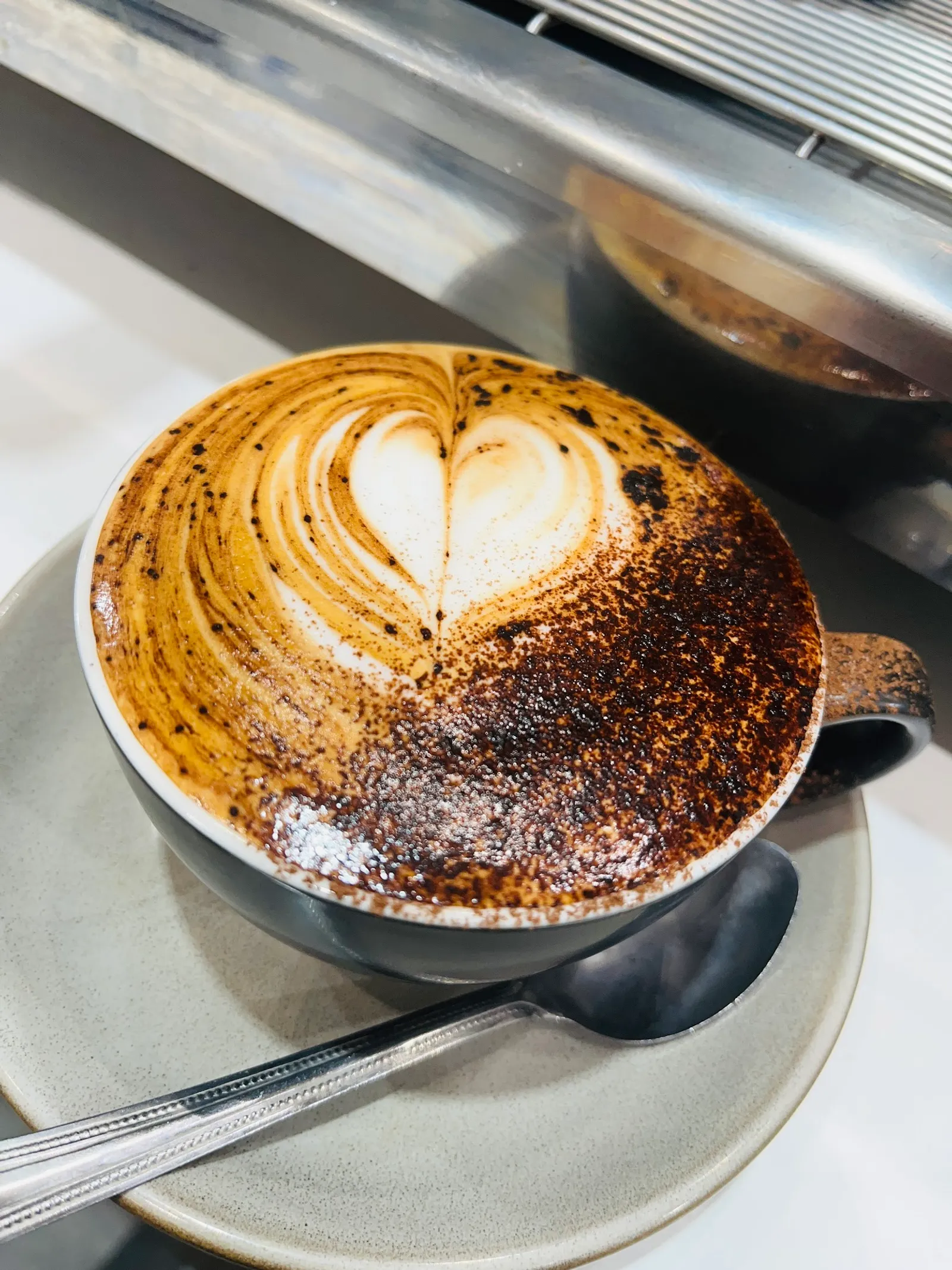 Mocha with heart latte art in dark ceramic cup with chocolate dusted foam