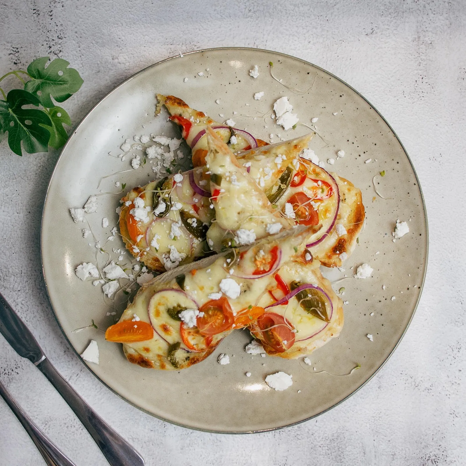 Cheesy open-faced focaccia toast with tomato, onion, jalapeno and feta on ceramic plate